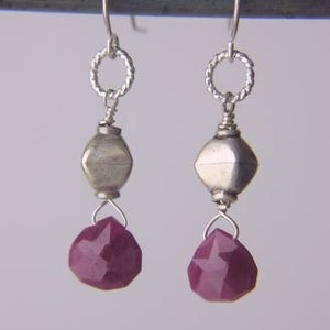 May include: A pair of silver dangle earrings with a faceted ruby gemstone drop. The earrings feature a silver bead and a twisted wire loop.