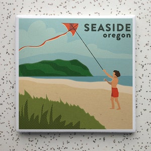 May include: A square tile featuring a vintage-style illustration of a beach scene. A person in red shorts flies a red kite with a long tail. The text "SEASIDE oregon" is displayed in a bold font against a blue sky.