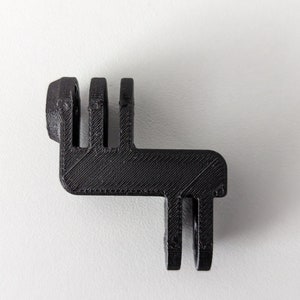 Puede incluir: Soporte de cámara negro impreso en 3D con base rectangular y tres ranuras verticales. El soporte tiene una parte superior curva con un punto de fijación circular. Sobre un fondo blanco.