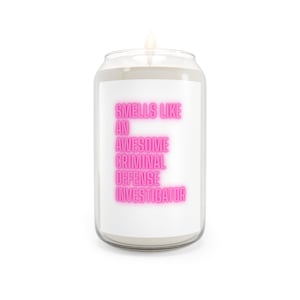 Può includere: Una candela in un barattolo di vetro trasparente con un'etichetta bianca che riporta il testo in rosa neon: SMELLS LIKE AN AWESOME CRIMINAL DEFENSE INVESTIGATOR. La candela ha uno stoppino visibile e contiene cera bianca in un contenitore a lattina.