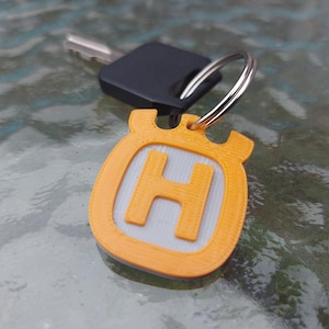 May include: A yellow keyring with a white "H" in the centre. The keyring is attached to a silver key ring.