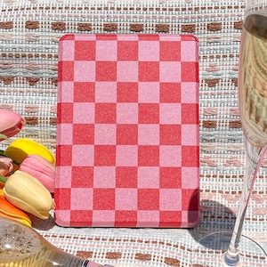May include: A pink and red checkered chopping board with a glass surface. The chopping board is on a patterned fabric surface. A bottle of wine and a glass of champagne are also on the surface.