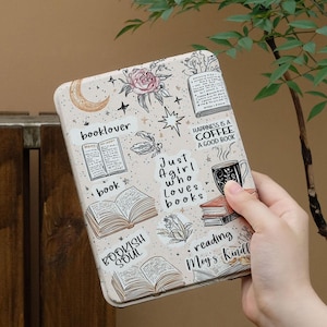 May include: A rectangular, beige book-themed case with illustrations of books, flowers, and text. The case features phrases like "booklover," "Just a girl who loves books," and "Happiness is a coffee, a good book."