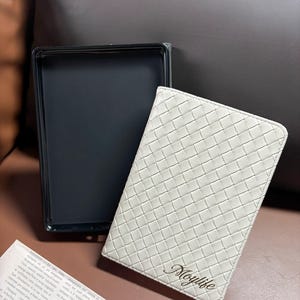 Puede incluir: Una libreta de cuero blanco con un patr&oacute;n tejido y la palabra "Moylife" grabada en letras doradas.
