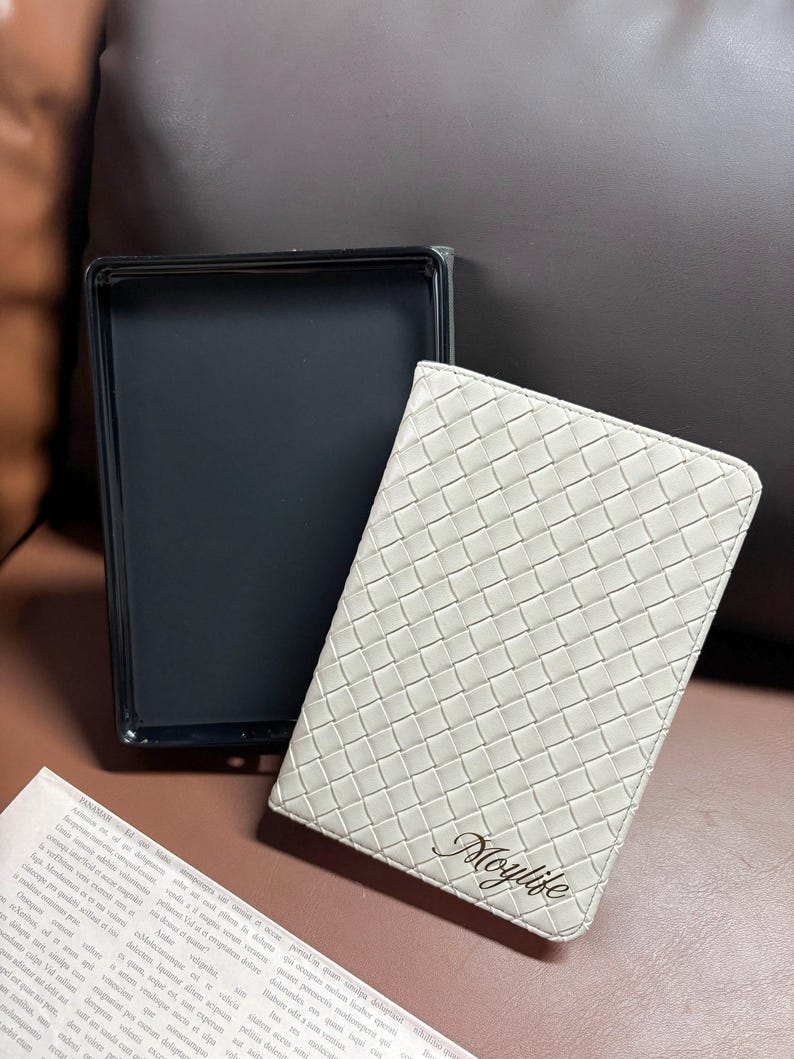 Puede incluir: Una libreta de cuero blanco con un patr&oacute;n tejido y la palabra "Moylife" grabada en letras doradas.