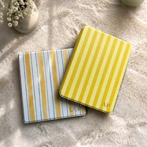 May include: Two rectangular cases with rounded corners. One case features vertical yellow and white stripes with the letters AP embossed in gold. The second case displays vertical yellow and light blue stripes with the letters LCR embossed in gold.