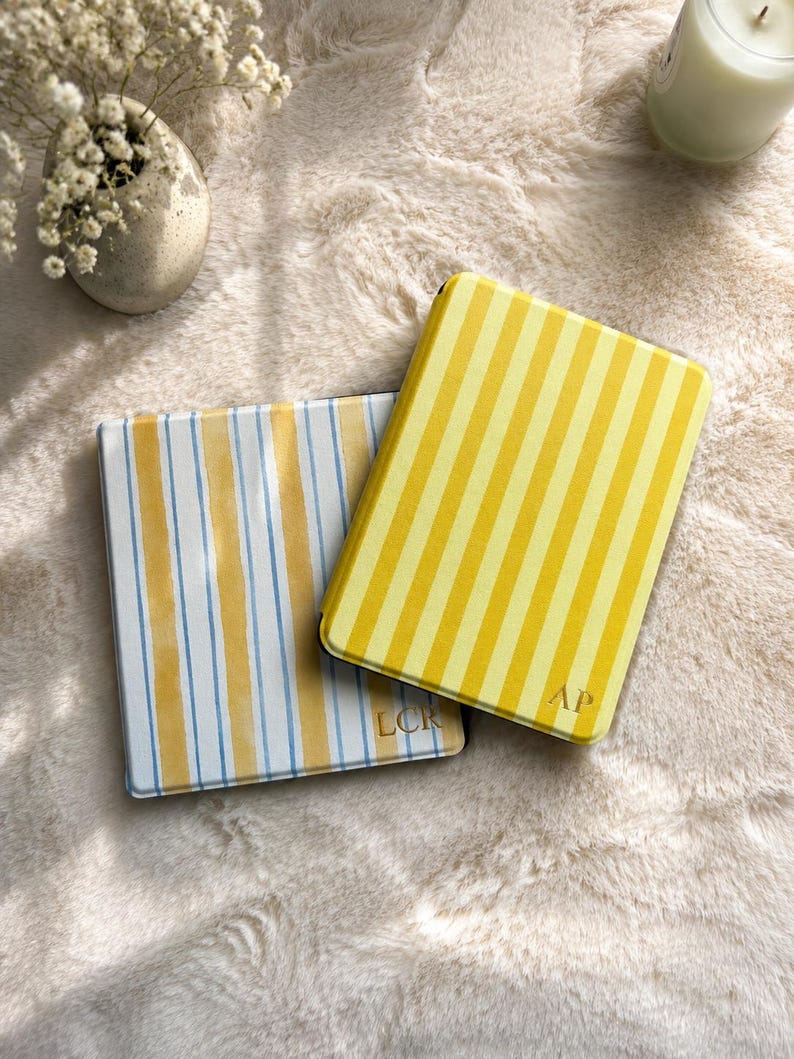 May include: Two rectangular cases with rounded corners. One case features vertical yellow and white stripes with the letters AP embossed in gold. The second case displays vertical yellow and light blue stripes with the letters LCR embossed in gold.