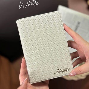 Puede incluir: Cartera de cuero blanca con un patr&oacute;n tejido y la palabra "Moylife" grabada en la parte delantera.