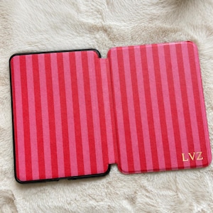 May include: A rectangular e-reader case featuring a vertical striped pattern in alternating shades of bright pink and dark red. The bottom right corner of the case displays the letters LVZ in a gold-colored font. The case is open and flat.