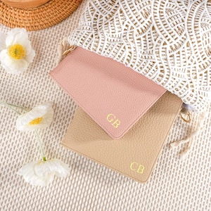 May include: Two leather pouches with gold lettering. The top pouch is pink and the bottom pouch is beige. Both pouches have the initials "CB" embossed on them.