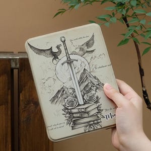 Könnte beinhalten: Eine rechteckige Metallbox mit einer Fantasy-Illustration. Das Design zeigt ein Schwert, Berge, Rosen, Bücher und geflügelte Kreaturen. Der Text enthält Sätze wie "You could nettle the door" und "To whatever end."
