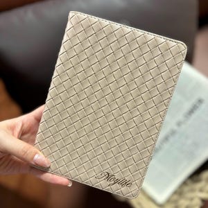 Puede incluir: Un cuaderno de cuero tejido beige con el nombre "Maylife" grabado en letras doradas.