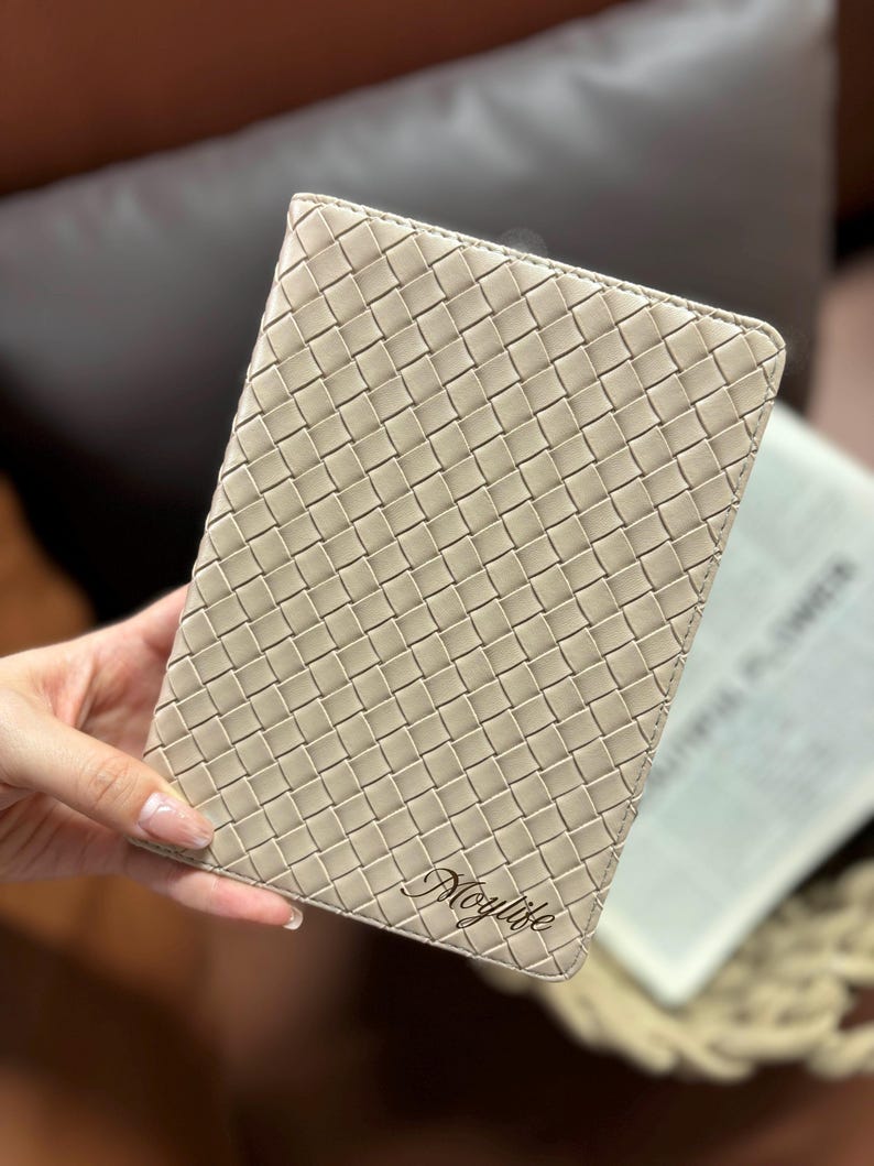 Puede incluir: Un cuaderno de cuero tejido beige con el nombre "Maylife" grabado en letras doradas.