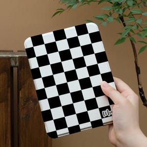 May include: A tablet case featuring a black and white chequered pattern. The case is held in a hand and has rounded corners. The lower right corner of the case has the word "Mox" written in a cursive font.