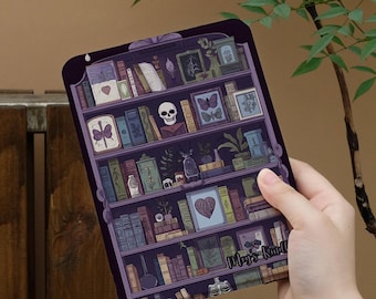 May include: A purple e-reader skin featuring a detailed illustration of a dark bookshelf filled with various books, framed butterfly art, a skull, potted plants, and a skeleton rib cage. The text "Meg's Kindle" is printed on the bottom shelf.