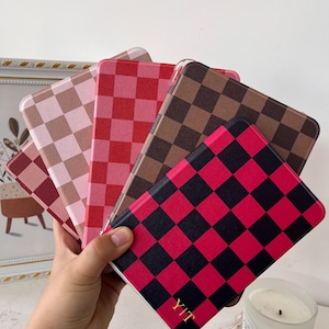 May include: A hand holds a fan of five square-patterned cases in shades of pink, red, brown, and black. The cases have a checkerboard design. The bottom case has the initials "YIT" in gold.