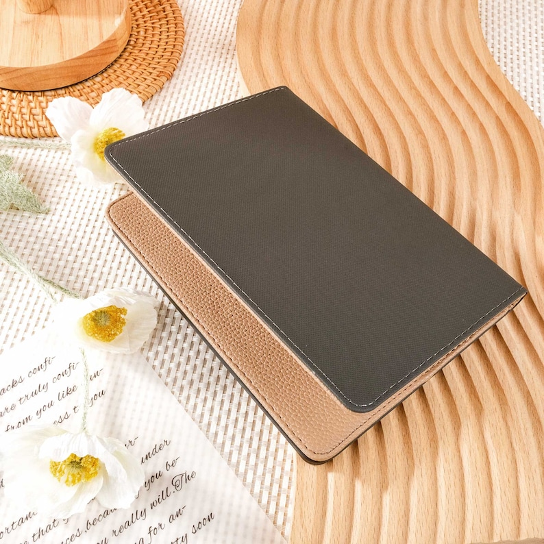 May include: A dark gray leather passport holder with a tan leather trim. The holder is closed and lying on a wooden surface.