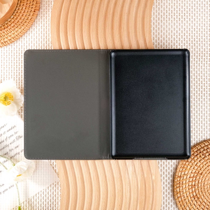 May include: A gray and black e-reader case with a textured cover and a black screen. The case is open and the screen is visible.