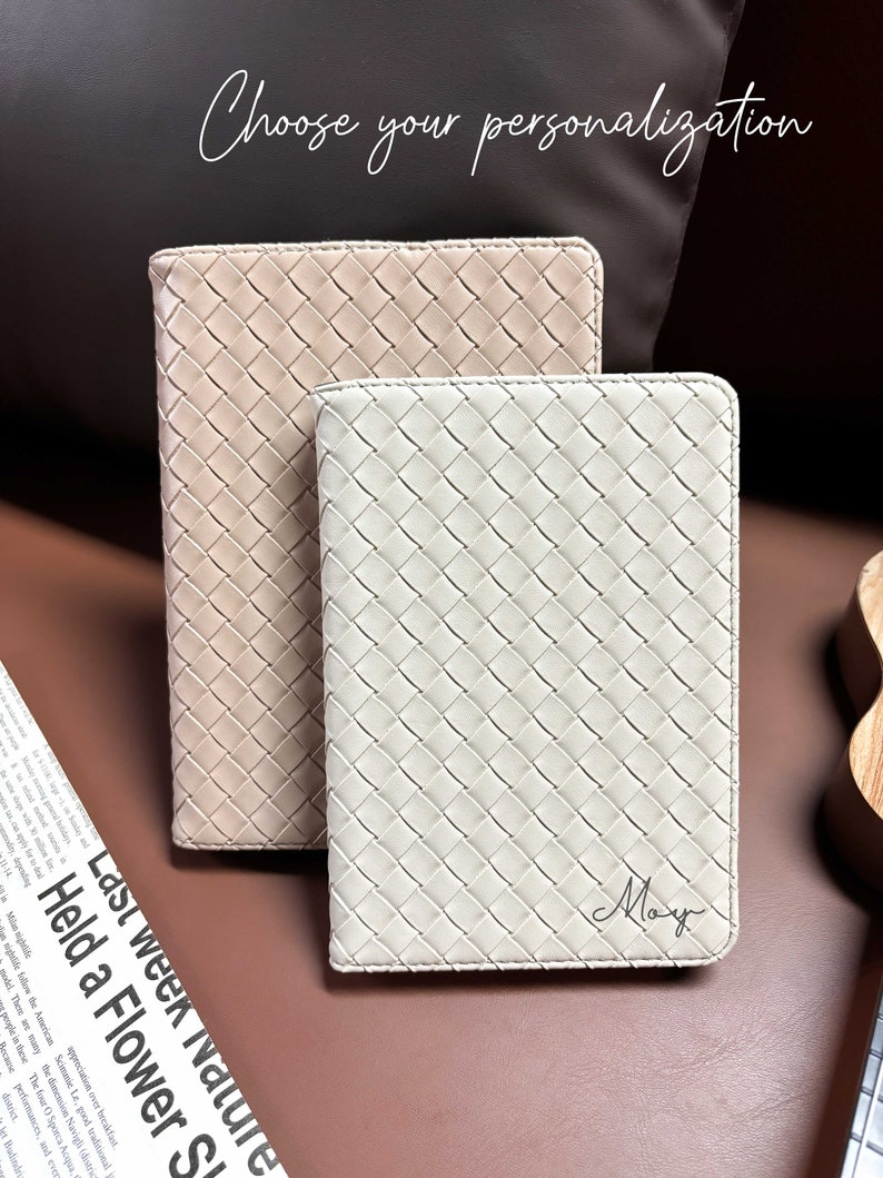 Puede incluir: Dos cuadernos de cuero trenzado, uno beige y otro blanco. El cuaderno blanco tiene el nombre "May" escrito en cursiva.