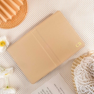 May include: A beige leather journal with the initials "CB" embossed in gold on the front cover.