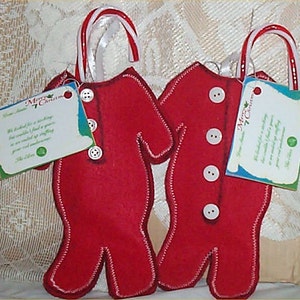 May include: Two red felt Christmas stocking ornaments shaped like pajamas, with white stitching and buttons. Each ornament has a candy cane handle and a tag that reads "Merry Christmas" and a poem.