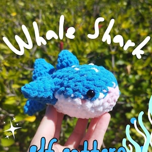 May include: A crocheted whale shark plush toy in blue and white with a pink belly. The toy is being held in a hand with the text "Whale Shark PDF Pattern" in the background.