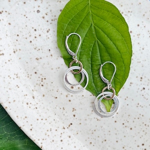 May include: Silver and gold hoop earrings with a layered design. The earrings have a simple hook closure.