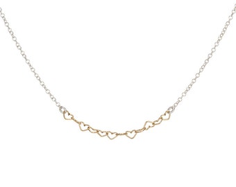 May include: A delicate necklace featuring a central row of seven small, interconnected gold-toned heart-shaped links, attached to a thin silver-toned metal chain on both sides, creating a continuous and elegant jewelry piece.