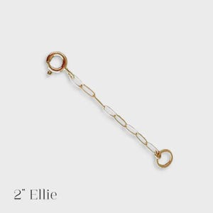 May include: A gold-colored chain extender, approximately 2 inches long, with a spring ring clasp at one end and a small ring at the other. The chain is composed of oval links. The text "2" Ellie" is at the bottom.
