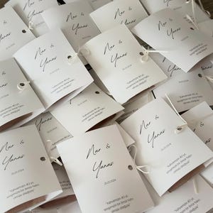 May include: A collection of white rectangular paper cards featuring the black printed names Nar & Yanas, the date 25.01.2024, and the Turkish text kahvemizin 40 yıl, sevgimizin bir &ouml;m&uuml;r hatırı olması dileğiyle. Each card has a small hole with white string.
