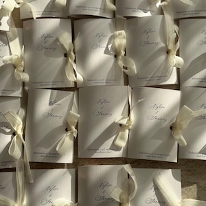 May include: A collection of white rectangular paper cards, each tied with a cream-colored ribbon. The cards feature the printed names Nefise & Sonmez in a cursive script, along with the text Kahvemizin 40 yıl, sevgimizin bir &ouml;m&uuml;r hatırı olsun.