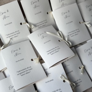 May include: A collection of white rectangular folded paper cards featuring the names Esra & Akin, the date 11.01.2025, and the Turkish text "Kahvemizin 40 yıl, sevgimizin bir &ouml;m&uuml;r hatırı olsun." Each card is secured with a thin white ribbon.