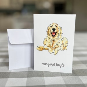 May include: A white card with a drawing of a golden retriever dog sitting with its tongue out. The dog is looking at the camera. The text "margaret boyle" is printed at the bottom of the card.