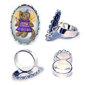 May include: A silver ring with a colorful patchwork cat wearing a purple dress and angel wings. The cat is holding a wand with a blue star on the end. The ring is set in an oval-shaped bezel.