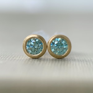 May include: A pair of gold stud earrings with blue gemstones. The earrings are round and have a smooth, polished finish.