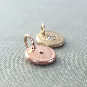 May include: Two gold charms, one with a small diamond in the center of a star design, and the other a plain disc with a small hole in the center.