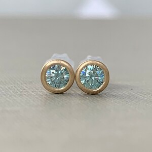 May include: A pair of gold stud earrings with a light blue round gemstone in each earring.