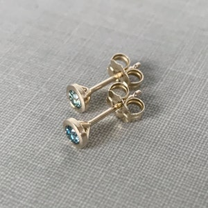May include: A pair of gold stud earrings with small, round, blue gemstones.