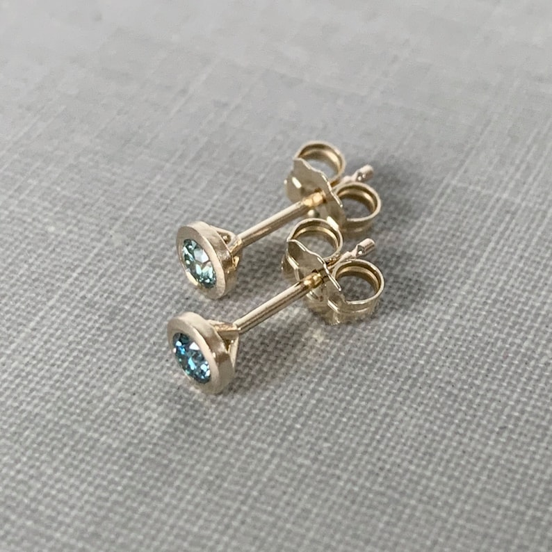 May include: A pair of gold stud earrings with small, round, blue gemstones.