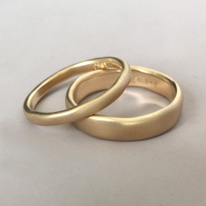 Op de afbeelding: Twee gouden trouwringen met een geborstelde afwerking. De ringen zijn op elkaar gestapeld. De bovenste ring heeft de inscriptie "585 14K".