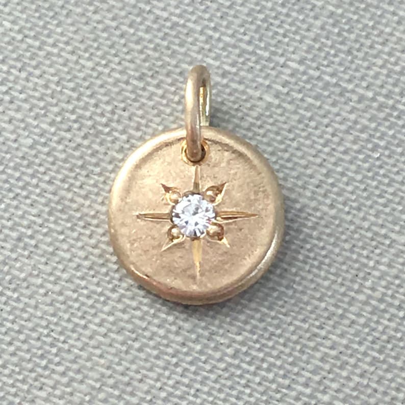May include: A gold charm with a small diamond in the center of a star design.