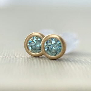 May include: A pair of gold stud earrings with blue gemstones. The earrings are round and have a smooth, polished finish.