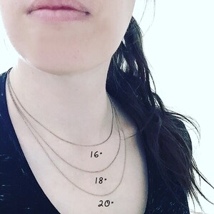 May include: Three silver chains of different lengths on a person's neck. The chains are labeled 16", 18", and 20".