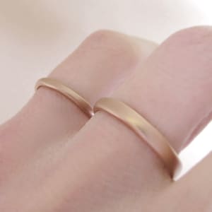 Op de afbeelding: Twee gouden trouwringen aan een vinger. De ringen zijn glad en hebben een afgerond profiel.