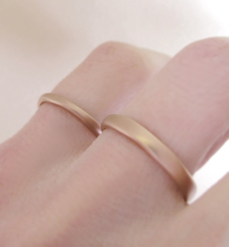 Op de afbeelding: Twee gouden trouwringen aan een vinger. De ringen zijn glad en hebben een afgerond profiel.