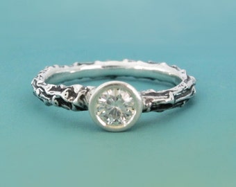 May include: A silver ring with a textured band that resembles a tree branch. A clear round gemstone is set in the center of the band.