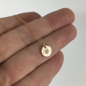 May include: A delicate gold necklace featuring a small, round pendant with a starburst design and a central diamond. The pendant hangs from a fine gold chain. The necklace is displayed against a neutral background.