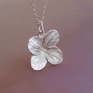 May include: A silver necklace featuring a dainty hydrangea flower pendant. The pendant is intricately detailed with realistic veins and textures.
