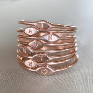 May include: A stack of eight rose gold rings with engraved letters and a heart. The letters are A, I, K, K, A, I, R, and a heart.