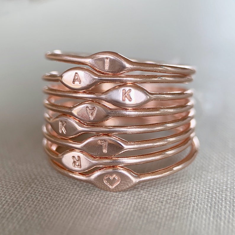May include: A stack of eight rose gold rings with engraved letters and a heart. The letters are A, I, K, K, A, I, R, and a heart.
